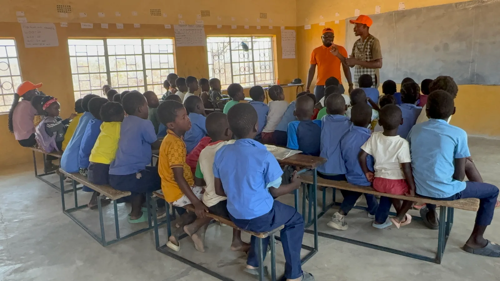 Inside-Out Community Ventures team members speaking to a full classroom of schoolchildren in Munyama