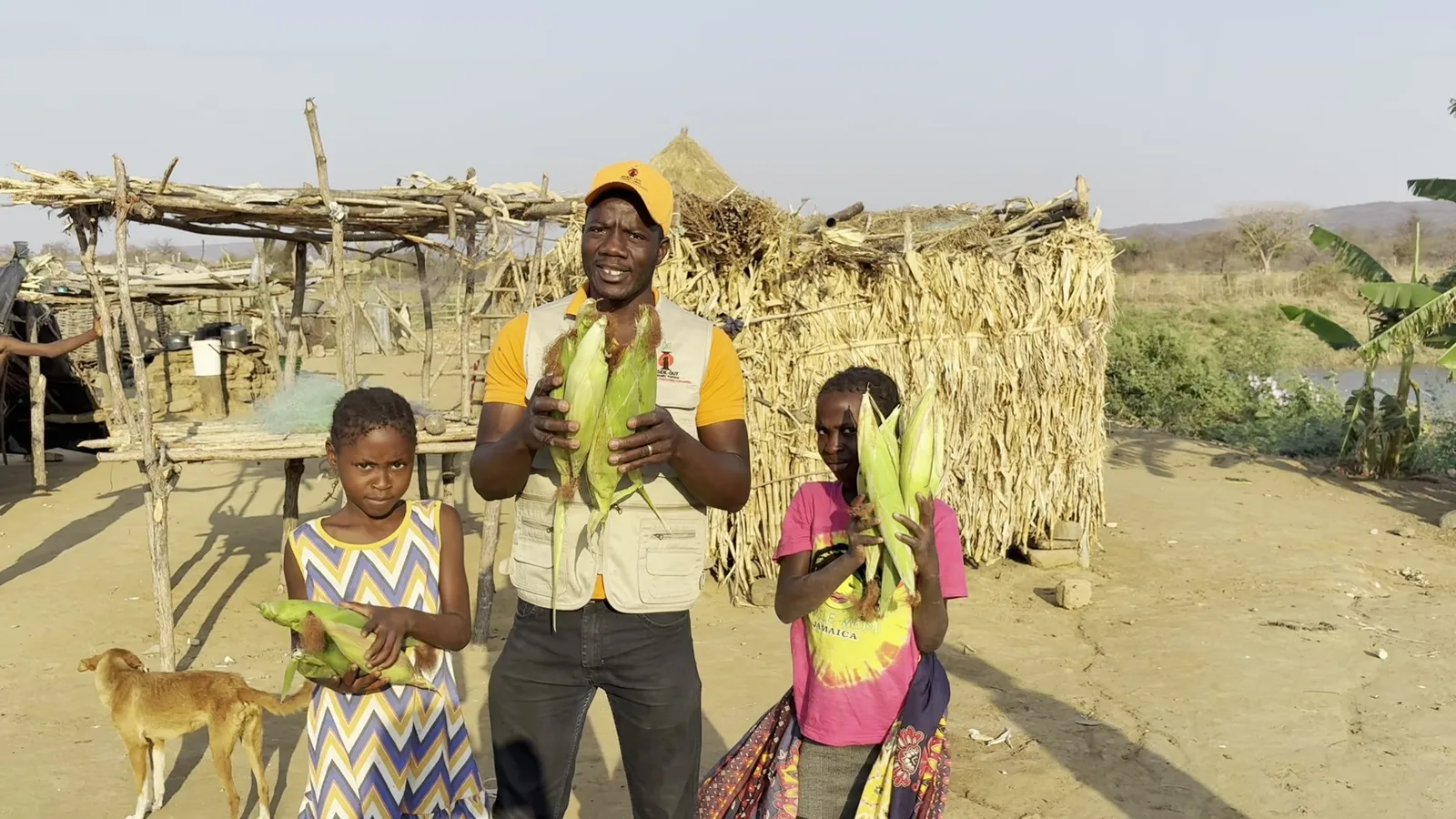 Fresh maize harvested in Munyama Village held up by children and an Inside-Out team member
