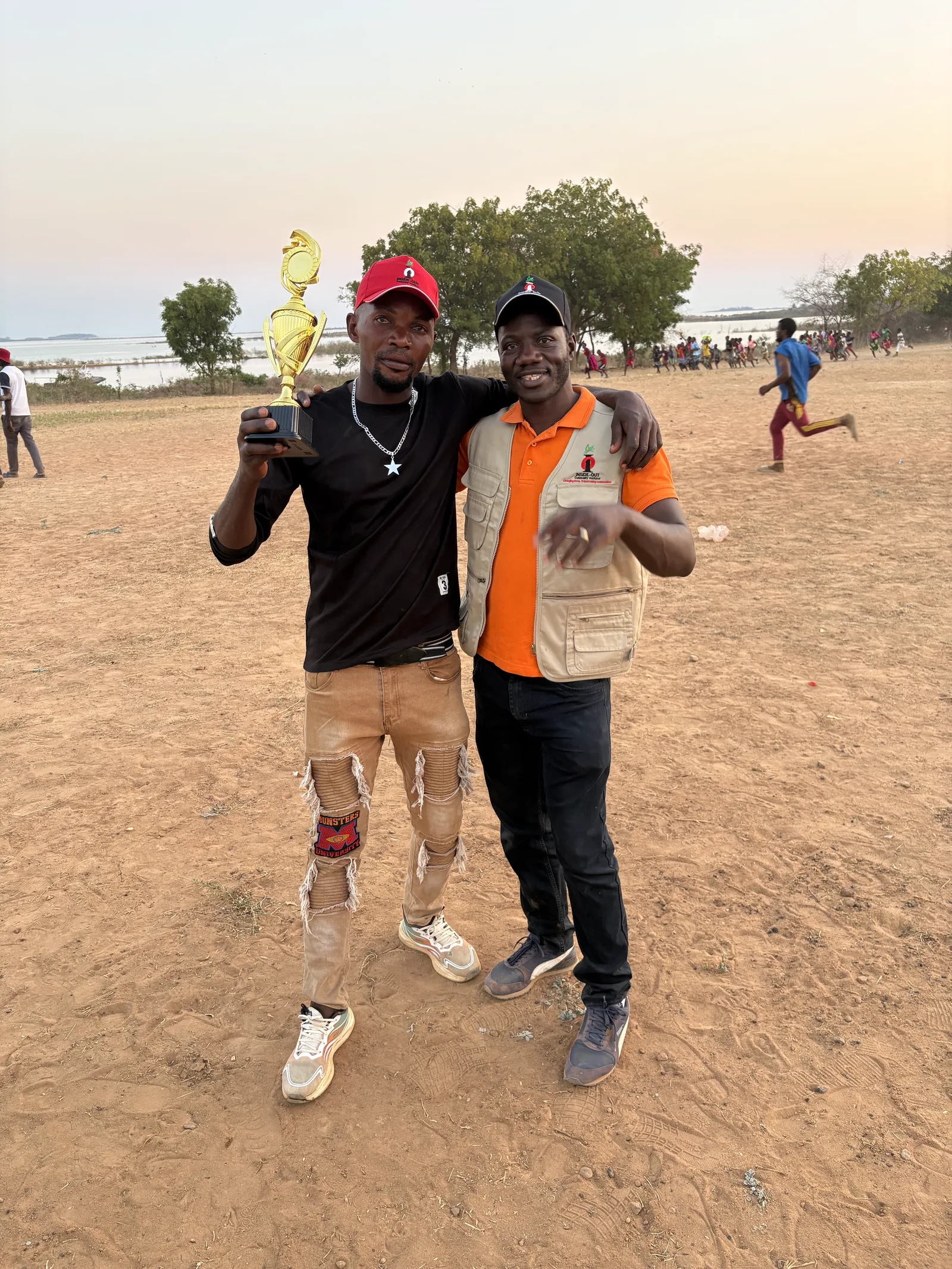 A competition winner holding his trophy alongside an Inside-Out Community Ventures team member in Munyama